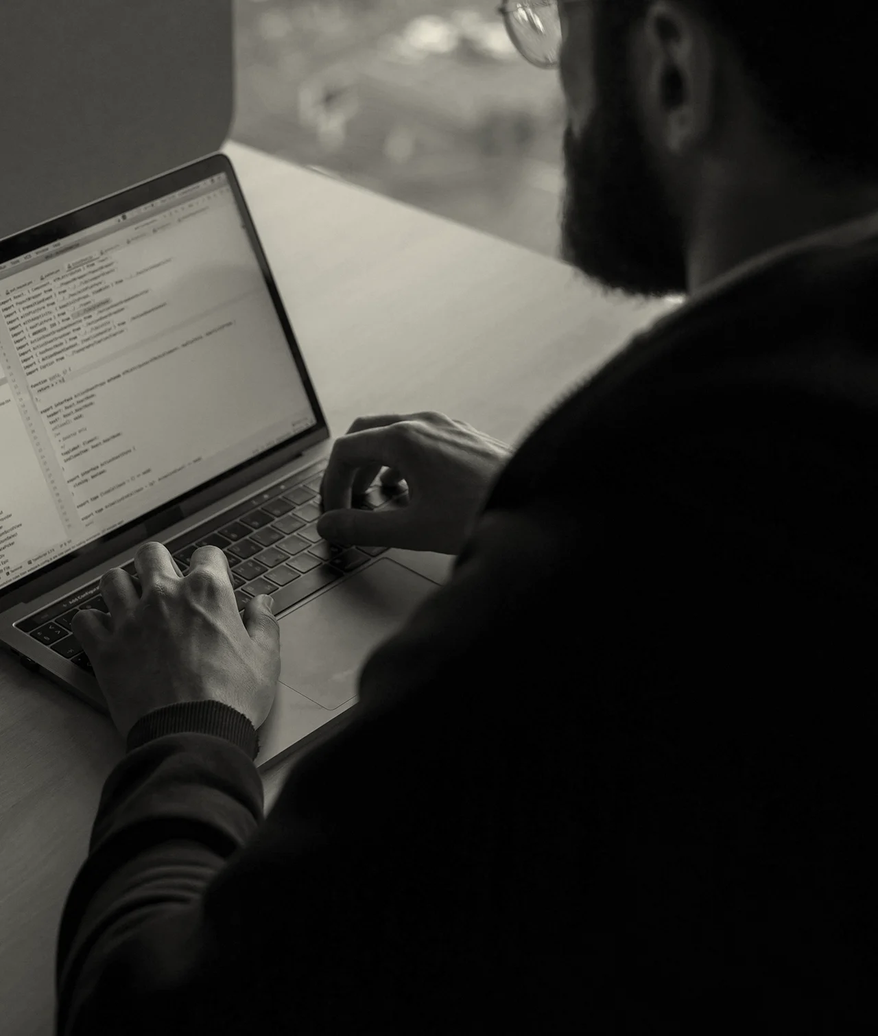 A man types code on his laptop while seated at a desk.